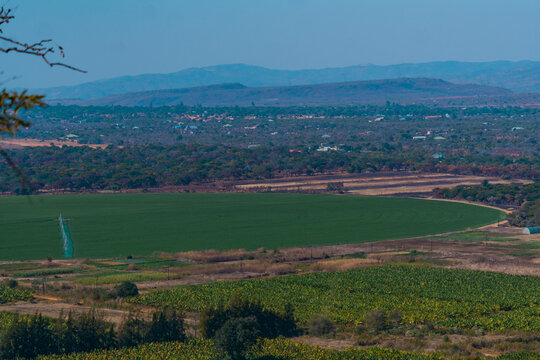 Kafue, Zambia - 19 July 2026: Aerial view of a large circular center pivot irrigation field with lush green crops surrounded by agricultural land and distant hills.