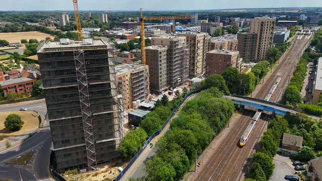 Stevenage, England, United Kingdom - 16 July 2026: Aerial view of Stevenage Railway Station with high-rise construction, cranes, and a train passing on the railway tracks.