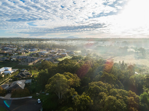 misty sunlit edge of town with houses backing onto trees