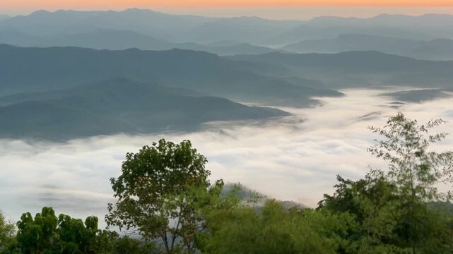 Smooth panning shot of a glowing sunrise and endless mountain ranges blanketed in morning fog at Doi Samer Dao, Thailand.