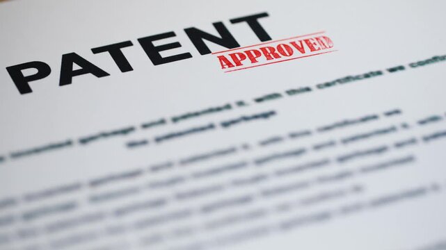 A close up view of a patent document being approved with a red stamp, signifying legal protection and innovation.