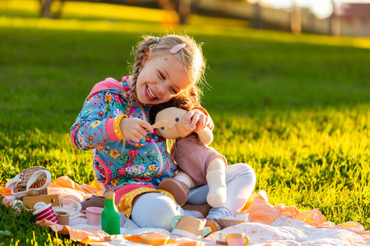 happy girl playing with wooden tea set toys and doll outdoors having a pretend picnic 