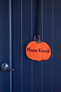 Welcoming Please Knock pumpkin sign on front door at Halloween