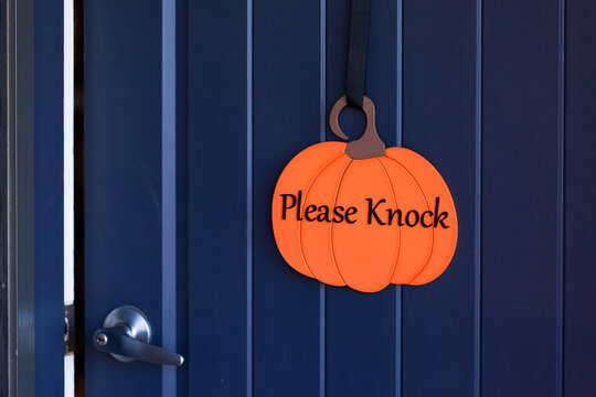 Welcoming Please Knock pumpkin sign on front door at Halloween