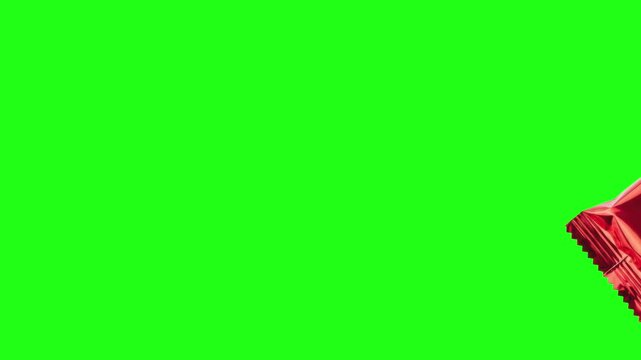 Red foil candy wrapper flying on green screen, metallic snack packaging floating in air, shiny plastic food pouch motion on chroma key background