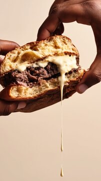A close perspective of hands lifting a cut burger with a crisp bun juicy filling and melting cheese in warm natural light with an appetizing rustic composition