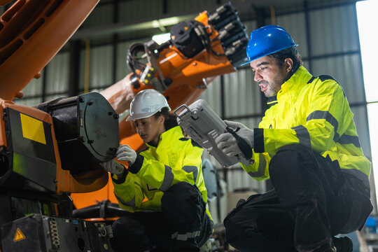 Industrial engineer inspecting robotic arm with diagnostic equipment in factory. Teamwork, industrial automation, predictive maintenance, manufacturing technology and quality control.