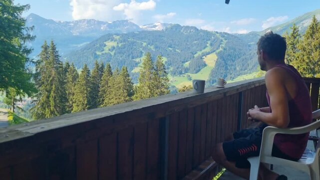 Man relaxing on a Swiss chalet balcony in Lenk, Simmental, enjoying a panoramic summer mountain view. A peaceful holiday moment capturing Alpine lifestyle, leisure, and Sunday tranquility, Switzerland