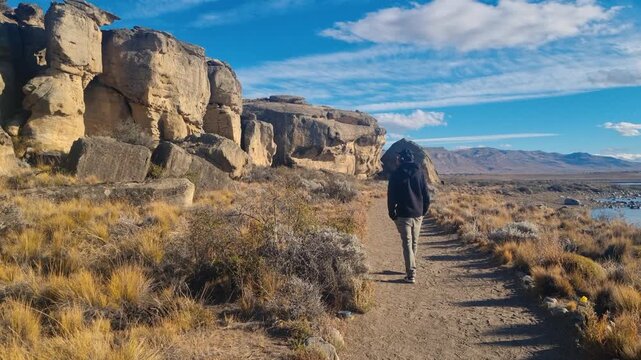 Solo traveler is walking along the shore of Lago Argentino between the lake and prehistoric rock caves at Punta Walichu near El Calafate, Argentina, Patagonia, in golden evening light