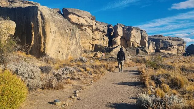 Man following an audio tour at Punta Walichu near El Calafate, Argentina, in golden evening light, walking along a path through a rocky Patagonian landscape beneath blue skies