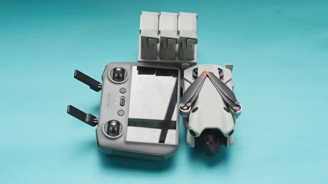 Hand placing folded mini drone next to its smart remote controller and battery hub on blue background