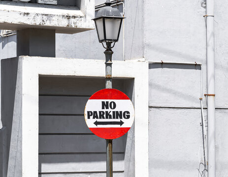 Close-Up of a red and white No Parking street sign with urban background.