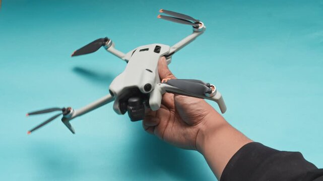 Hand powering on and lifting unfolded mini drone against cyan background