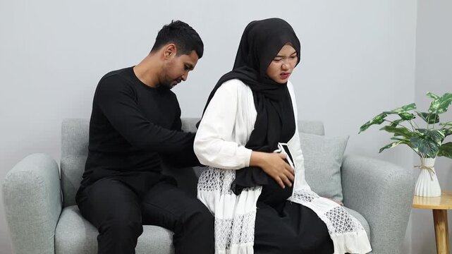 Husband gives pregnant wife back massage during pregnancy sitting on sofa at home