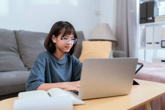 Young woman focuses on her laptop while working in a cozy living room during the day