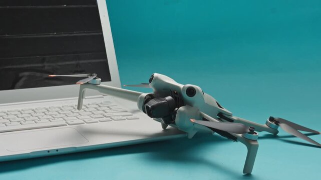 Hand placing modern mini drone next to open white laptop against cyan background