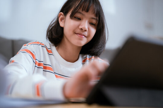 Young girl studying and taking notes while using a tablet at home in a cozy living room