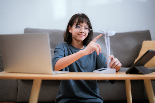 Young girl engages with a small wind turbine model at home, showcasing her interest in renewable energy and technology