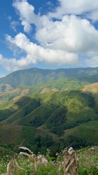 Panoramic landscape of lush green mountain ranges and valleys under a partly cloudy blue sky in Sapan, Nan, Thailand.