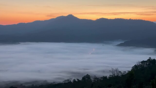 Cinematic panoramic sunrise revealing a dense blanket of morning fog rolling through the mountain valley in Pong, Phayao, Thailand.