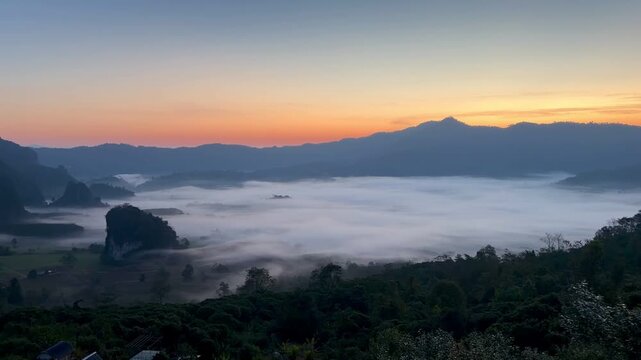 Cinematic panoramic sunrise revealing a dense blanket of morning fog rolling through the mountain valley in Pong, Phayao, Thailand.
