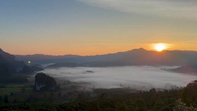 Cinematic panoramic sunrise revealing a dense blanket of morning fog rolling through the mountain valley in Pong, Phayao, Thailand.