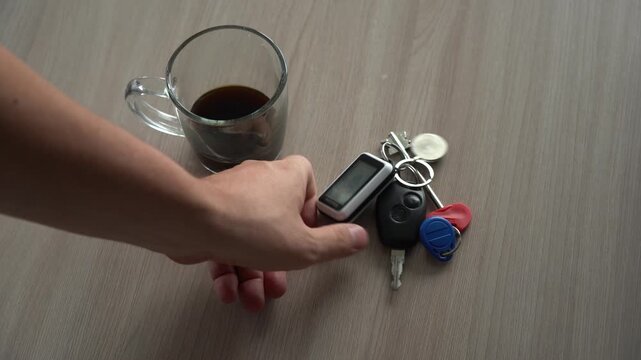 A scene of a calm morning: a cup of coffee and a ring of car keys lie on a light wooden table, symbolizing daily activities and the beginning of a new day. A mans hand picks up the keys from the table