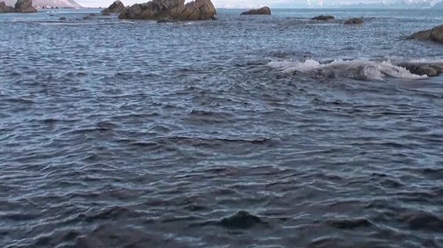 Extreme journey navigates vast Arctic Ocean. Cold waves gently lap at ancient rock formations. Sudden splash breaks calm, revealing moment of dynamic action amidst remote polar expanse.
