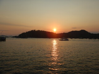Fototapeta premium Tourist boat sailing on ocean water during vibrant golden sunset near tropical island shore