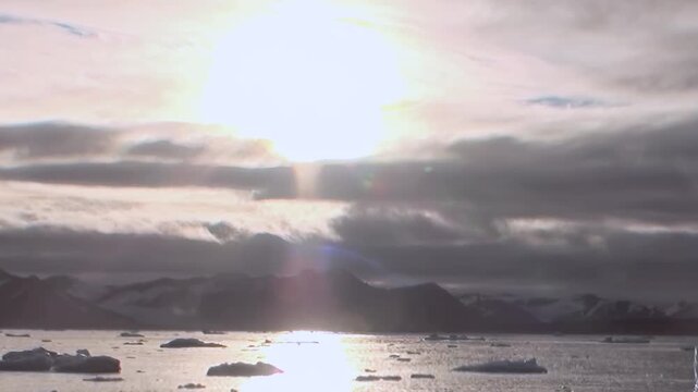 Expedition crosses vast Arctic Ocean, unveiling majestic polar panorama. Brilliant sunlight streams through clouds, illuminating floating icebergs and sparkling waters during this extreme journey.