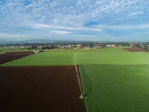 Irrigation sprinkler alongside lush green paddock with tilled land of fertile soil