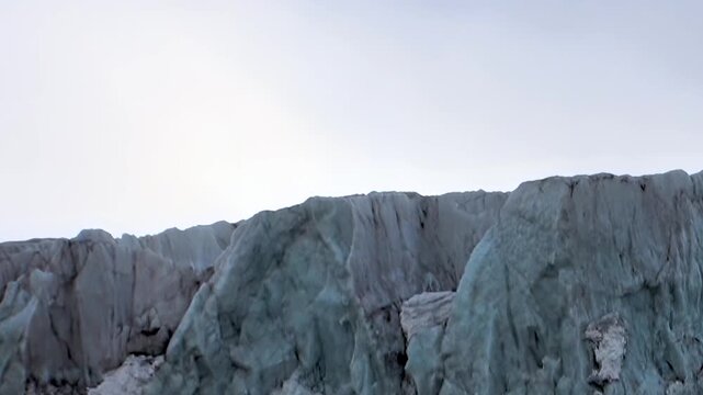 Witness the breathtaking grandeur of a towering Arctic glacier. Its ancient, turquoise ice wall, carved by relentless forces, stands majestically under soft daylight, a colossal frozen wonder.