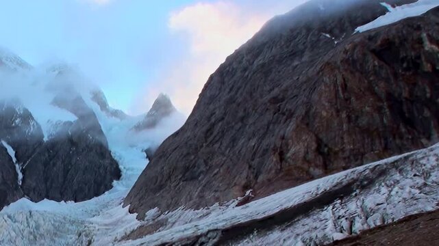 Witness the majestic flow of an ancient glacier nestled within the towering, stark mountains of the Arctic. Clouds drift across the cold sky at a serene moment in this remote, icy wilderness.