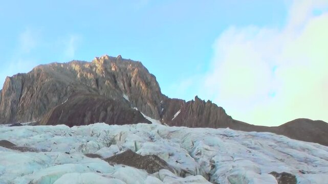 Immense glacier sprawls across the Arctic landscape under a bright daytime sky. Majestic, rugged mountains tower behind the vast, ancient ice field, shimmering in the northern light.