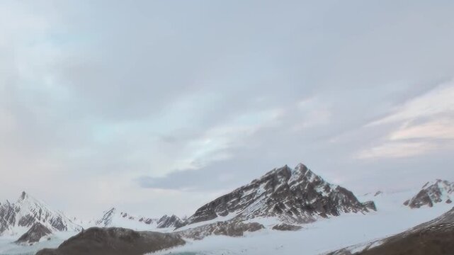 Witness the breathtaking grandeur of an ancient glacier nestled among towering, snow-dusted peaks in the pristine Arctic.