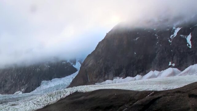 Witness the breathtaking expanse of an Arctic glacier, its textured surface stretching between towering, cloud-kissed mountains.