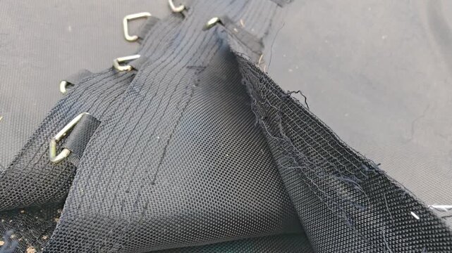 Torn and damaged trampoline mat with a hole in the mesh fabric, worn out sport equipment closeup, safety defect, repair or replacement needed.