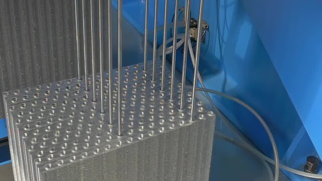 Silver needles glide into aligned holes of a solid block, showcasing engineering precision and mechanical movement during an automated assembly session in a modern factory.
