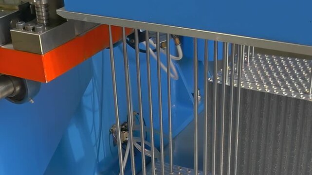 Precision steel wires descend through vibrant blue industrial frame to slice through delicate foam blocks with steady mechanical motion inside quiet manufacturing plant during bright afternoon hours