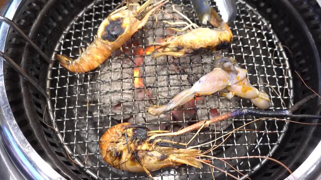 Grilled prawns and frog legs on charcoal grill at street market. Symbolizes Asian street food and seafood cuisine. Ideal for culinary and travel content