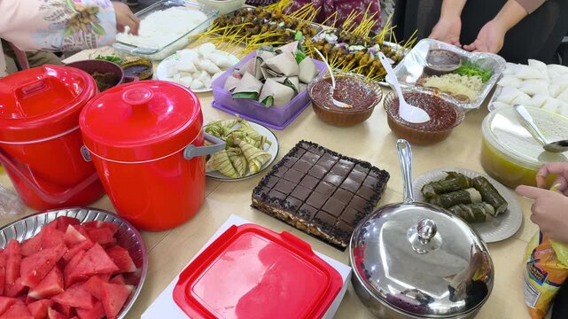 A festive Hari Raya feast features traditional Malaysian dishes on display. Served foods include compressed rice cakes, peanut sauce, and satay skewer options. Guests celebrate Eid with rich local fla
