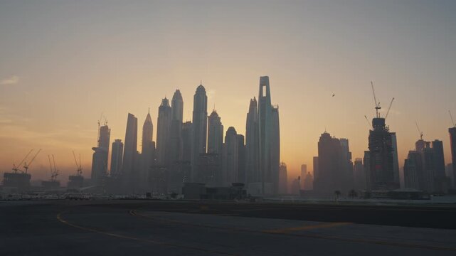 A wide establishing shot capturing the Dubai Marina skyline bathed in warm golden hour light during early morning. Soft, glowing sunlight.