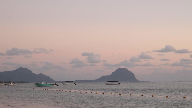 coastal mountains at dusk overlooking Flic en Flac beach, Mauritius. The sky transitions to soft violet and orange hues, creating a tranquil tropical atmosphere.
