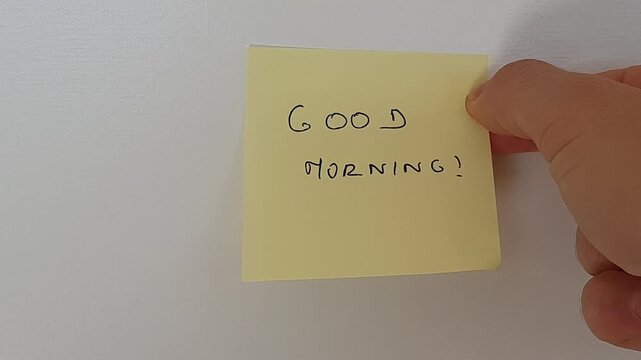Hand placing sticky note with Good Morning text on white wall