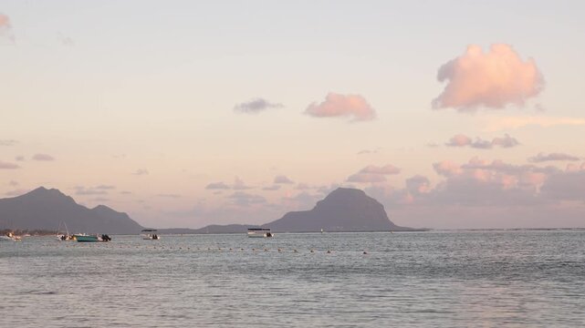 Panoramic twilight scenery overlooking calm coastal waters and distant mountain silhouettes during sunset at Flic en Flac, Mauritius, featuring scattered moored boats.
