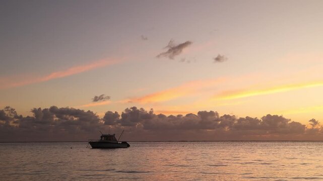 Vibrant sunset glowing over the calm ocean horizon at Flic en Flac, Mauritius, with a silhouette of a small boat floating peacefully on the evening tide.