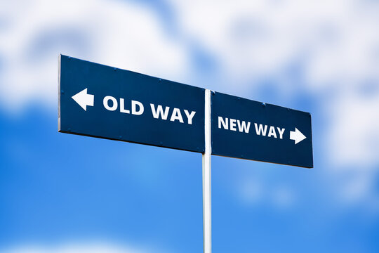 Dark directional sign showing old way and new way against blue sky