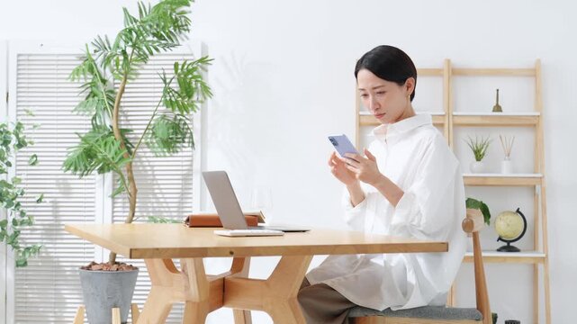通帳とスマホを見ながら悩むミドル女性。貯金、節約、ローン、アプリ、家計、銀行、給料、不満、心配、不安