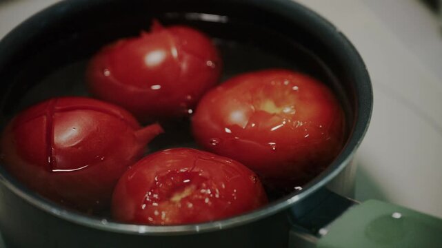 Close up shot of fresh red tomatoes blanching in boiling water in pot.