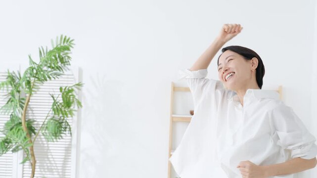部屋でガッツポーズするミドル女性。嬉しい、喜ぶ、楽しい、元気、ポジティブ、リラックス、笑顔、満足